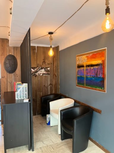 Coin d'une salle avec des chaises noires, une table blanche et une peinture colorée au mur.